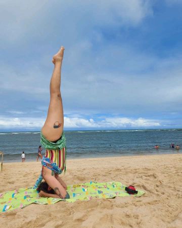 xRainbow Rafa Beleze doing a head stand in the sand on a beach.